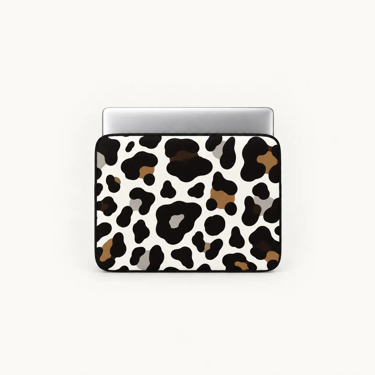 A laptop sleeve featuring a cow print pattern in black, brown, and gray on a white background, shown with a silver laptop on top against a light off-white background.