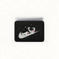 A black laptop sleeve featuring a graphic of an astronaut floating on a gray Nike swoosh against a black space background with white stars, shown on a silver laptop against a white studio background.