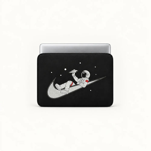 A black laptop sleeve featuring a graphic of an astronaut floating on a gray Nike swoosh against a black space background with white stars, shown on a silver laptop against a white studio background.