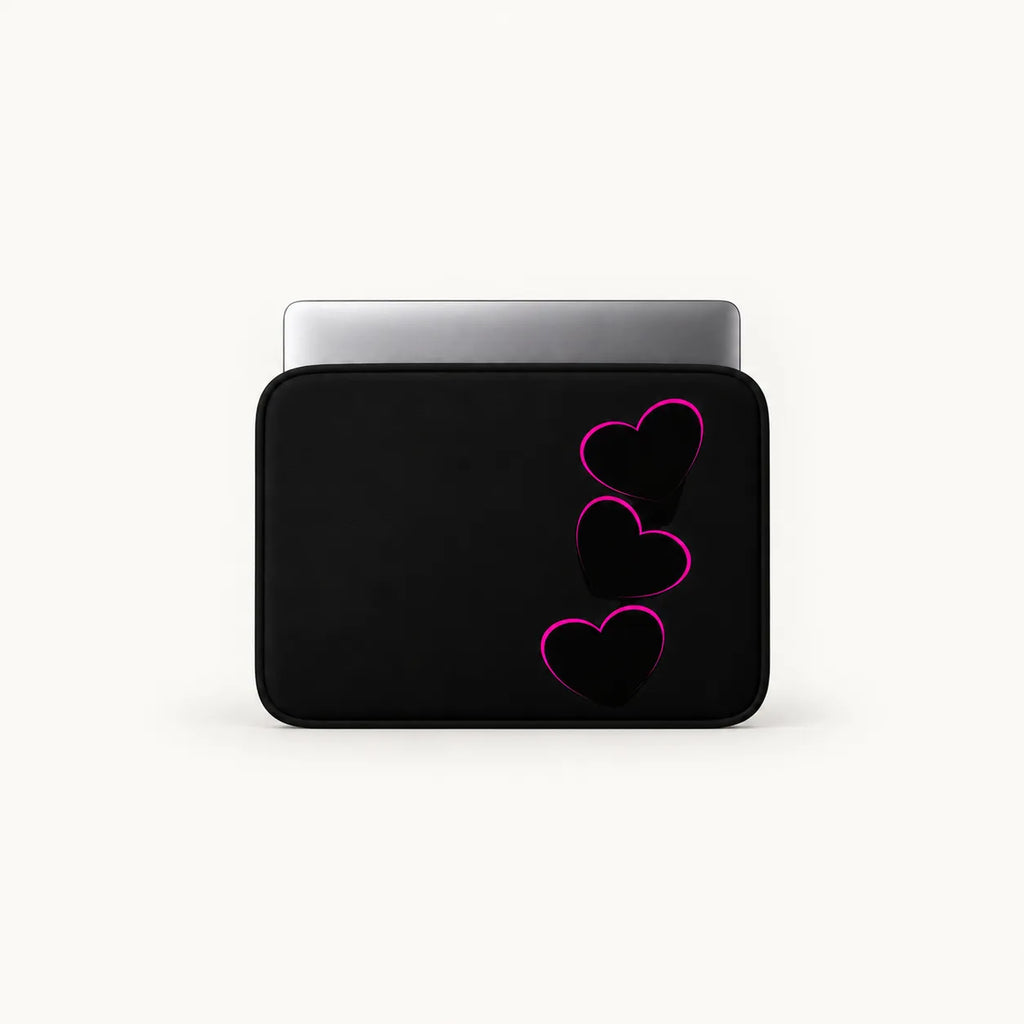 A black laptop sleeve with three stacked pink-outlined hearts on the front, shown with a silver laptop partially inserted, against a clean off-white background.