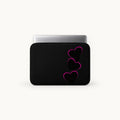 A black laptop sleeve with three stacked pink-outlined hearts on the front, shown with a silver laptop partially inserted, against a clean off-white background.