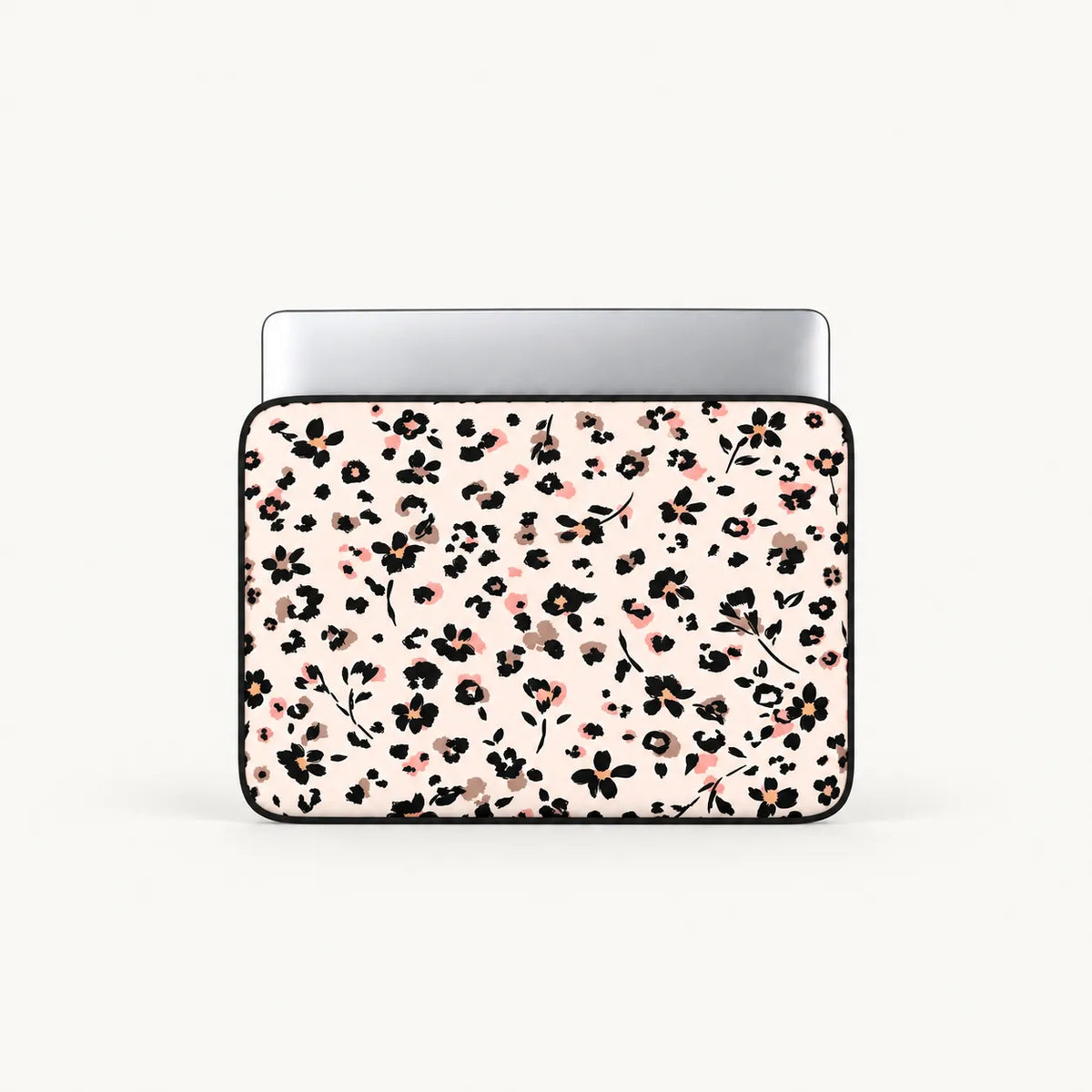 A laptop sleeve with a dense black and pink floral pattern on a light cream background, shown with a silver laptop inside against a light gray studio background.