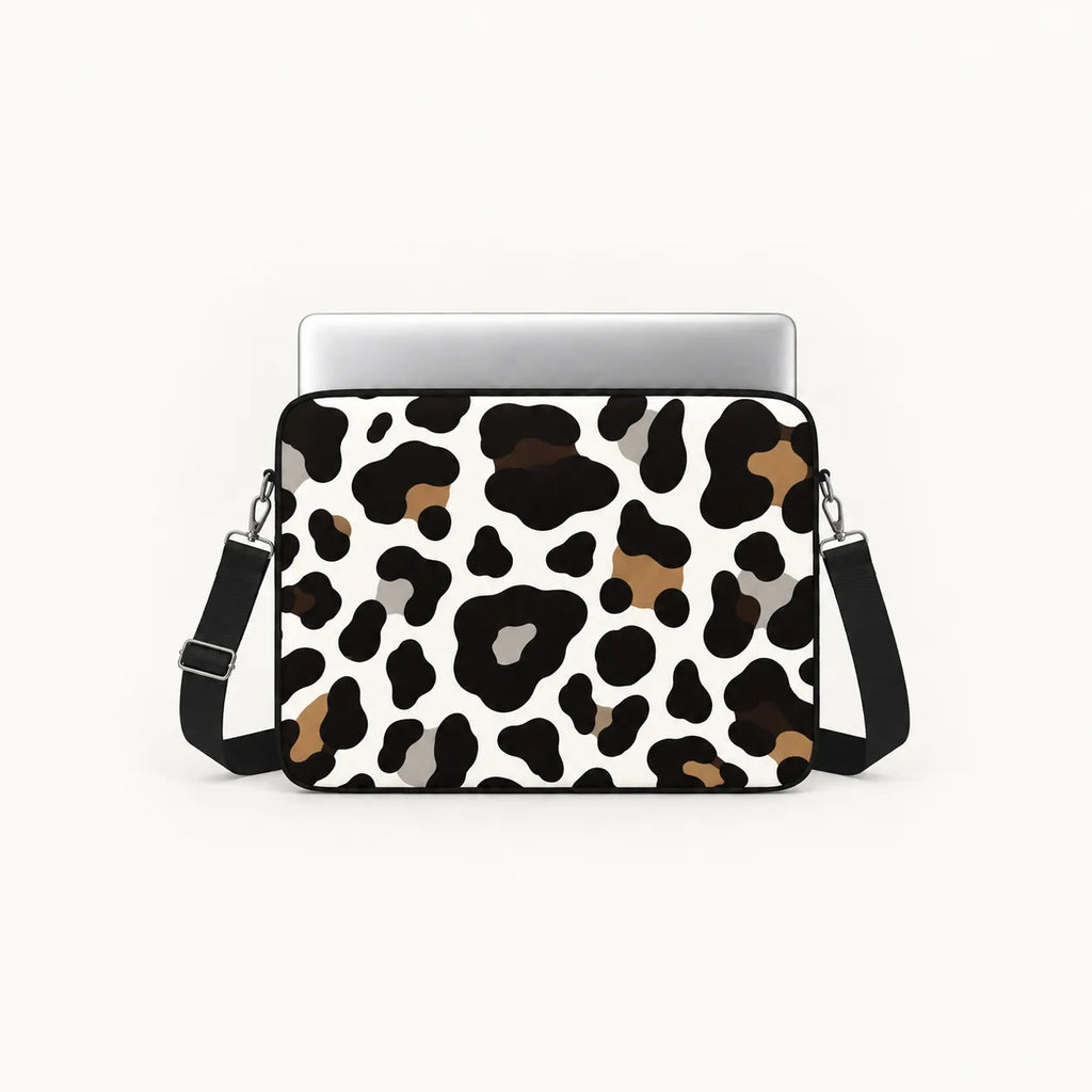 A laptop sleeve featuring a black, brown, and gray leopard print pattern on a white background, shown with a silver laptop and a black shoulder strap against a light off-white background.