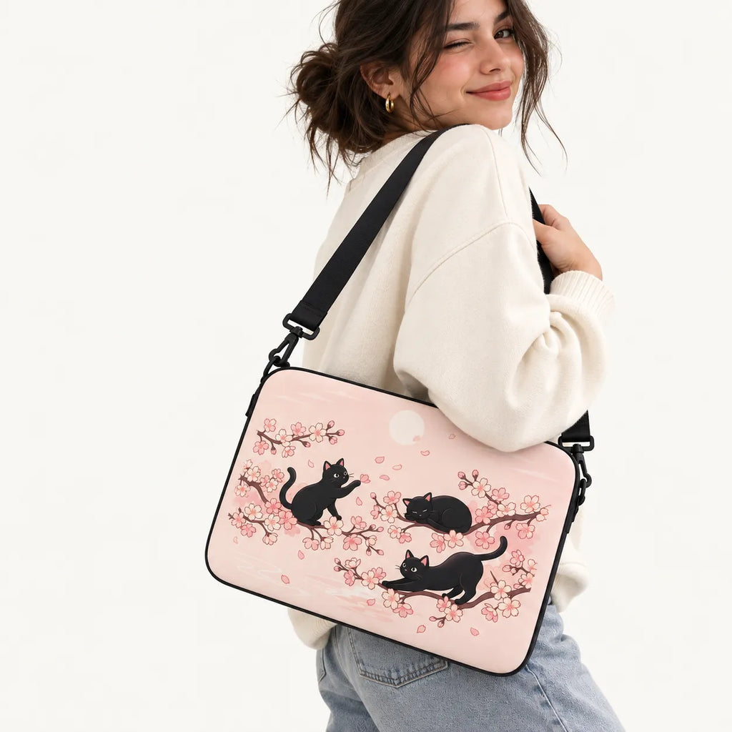 Three black cats playing among Japanese cherry blossom sakura branches on a pastel pink padded laptop sleeve by SLEEVER