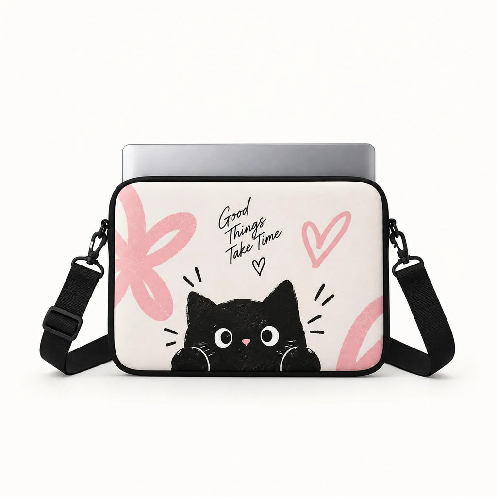 A laptop sleeve featuring a cute black cartoon cat peeking up from the bottom, with pink abstract shapes, the handwritten text 'Good Things Take Time', and a pink heart. A silver laptop is shown inside the sleeve, which has a black adjustable shoulder strap, photographed on a clean white background.