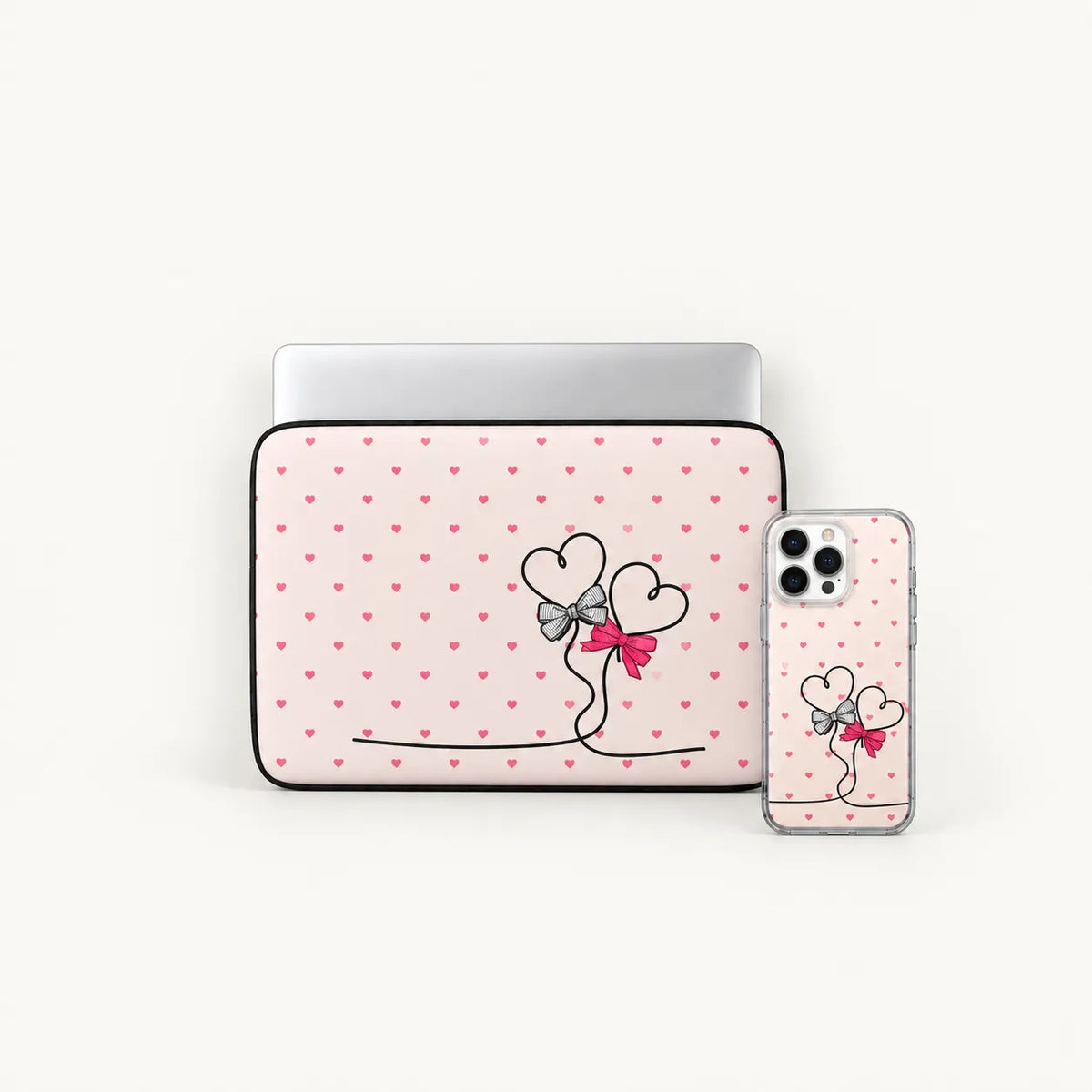 A laptop sleeve and a smartphone case shown on a clean white background. Both pieces feature a light pink base with small darker pink hearts, a black line-art illustration of two heart figures holding a pink bow, and a silver metallic trim.