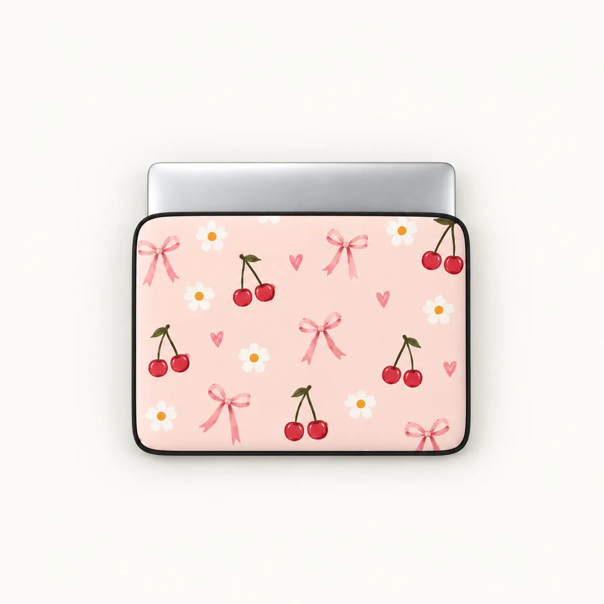 A laptop sleeve with a light pink background, decorated with a pattern of red cherries, white daisies, pink bows, and small pink hearts, shown on a silver laptop against a light off-white background.