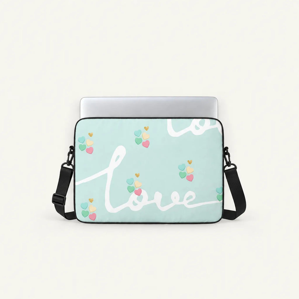 A mint green laptop sleeve with a black shoulder strap, featuring a white cursive 'love' script and small pastel heart balloon motifs, shown with a silver laptop on a light cream background.