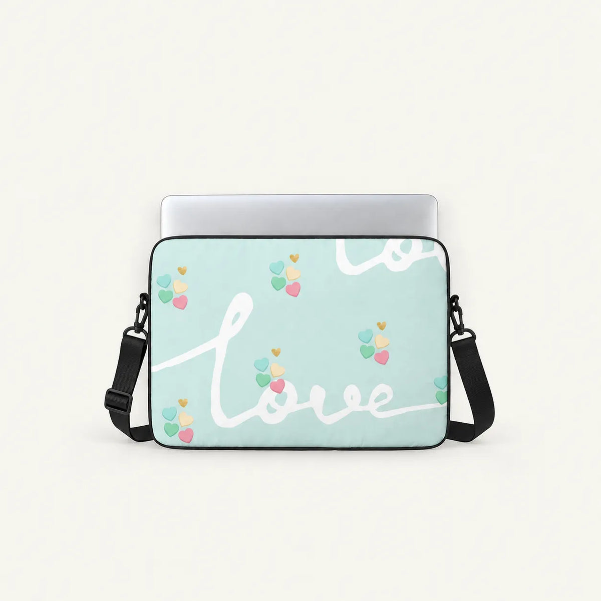 A mint green laptop sleeve with a black shoulder strap, featuring a white cursive 'love' script and small pastel heart balloon motifs, shown with a silver laptop on a light cream background.