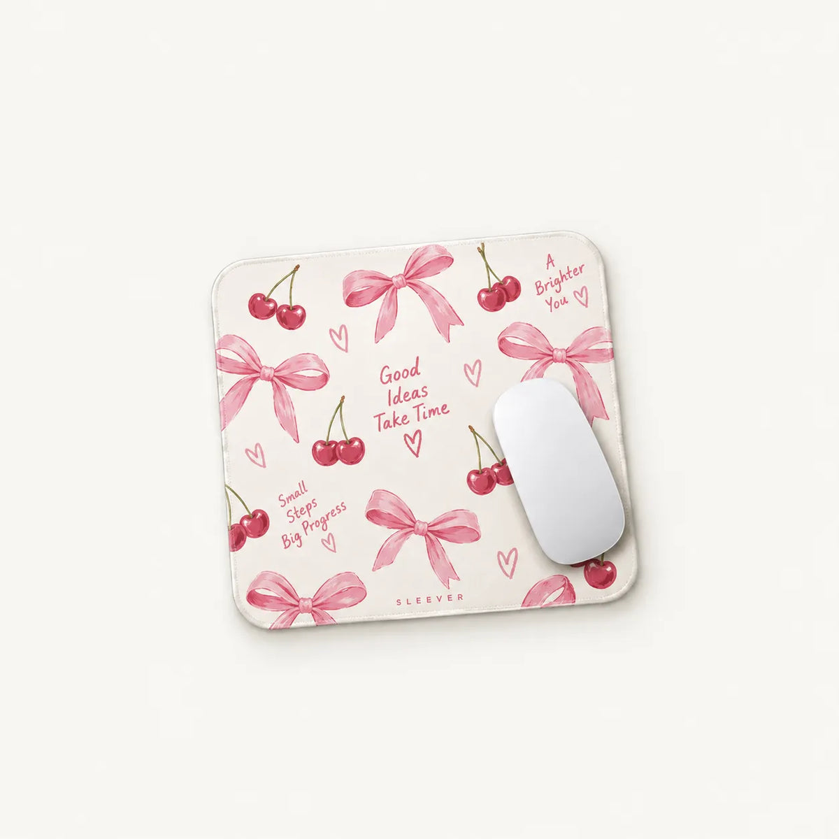 A square mouse pad with a pink cherry and bow pattern on a cream background, shown with a white computer mouse on a light off-white background. The mouse pad features the brand name 'SLEEVER' at the bottom.