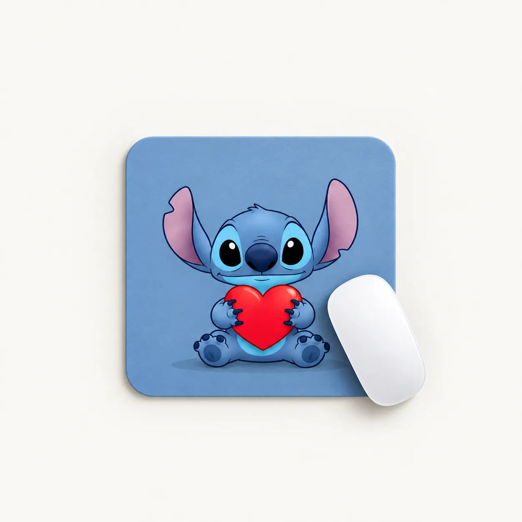 A square mouse pad with rounded corners featuring a blue cartoon character holding a red heart, shown on a light beige background with a white computer mouse partially overlapping it.