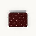 A laptop sleeve with a dark red background and a repeating pattern of small white bows, shown with a silver laptop inserted on a light gray background.