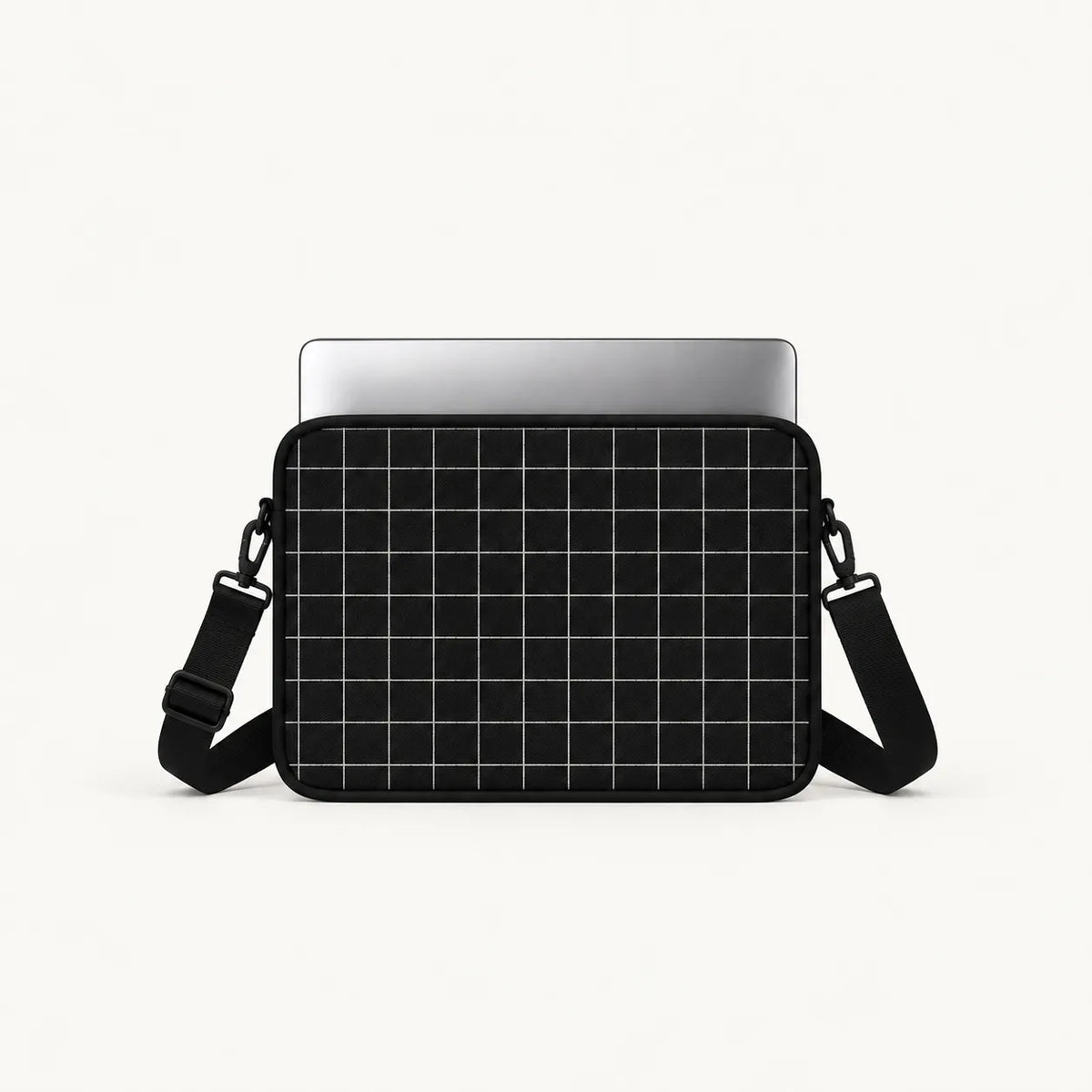 A black laptop sleeve with a white grid pattern, shown with a silver laptop inserted and a black adjustable shoulder strap, on a clean white background.