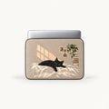 "SLEEVER 'Cozy Black Cat' laptop sleeve featuring an illustration of a black cat lounging on a bed in warm sunlight."   