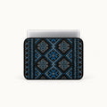 A laptop sleeve featuring a blue and black geometric tribal pattern, shown with a silver laptop inserted on a clean white background.