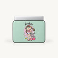 A laptop sleeve with a light mint green background and a colorful cartoon girl graphic, shown with a silver laptop partially inserted. The graphic includes the text 'Feebee' and 'BUZZ BUZZ BAIL!'.