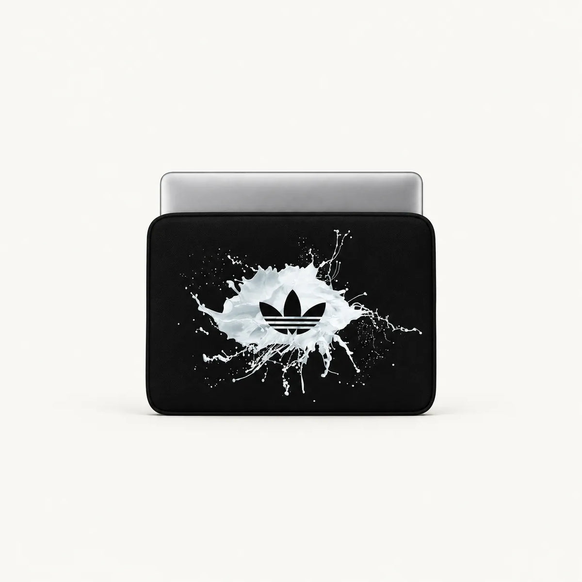 A black sleeve or cover with a white paint splatter graphic and a black Adidas trefoil logo in the center, shown on a silver laptop against a light gray background.
