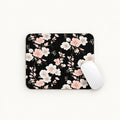 A rectangular mouse pad with a black background and a delicate pink and white floral pattern, shown on a clean white surface with a white computer mouse resting on the right side.