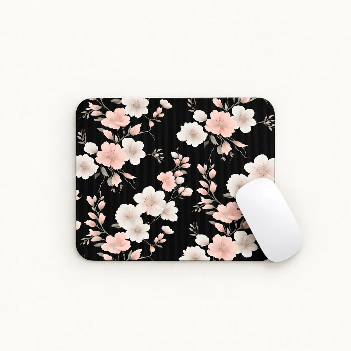 A rectangular mouse pad with a black background and a delicate pink and white floral pattern, shown on a clean white surface with a white computer mouse resting on the right side.
