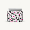 A laptop sleeve featuring a Paris-themed pattern with black cat faces, Eiffel Towers, pink hearts, and the phrase 'Je T'Aime' on a white background, shown with a silver laptop inserted.