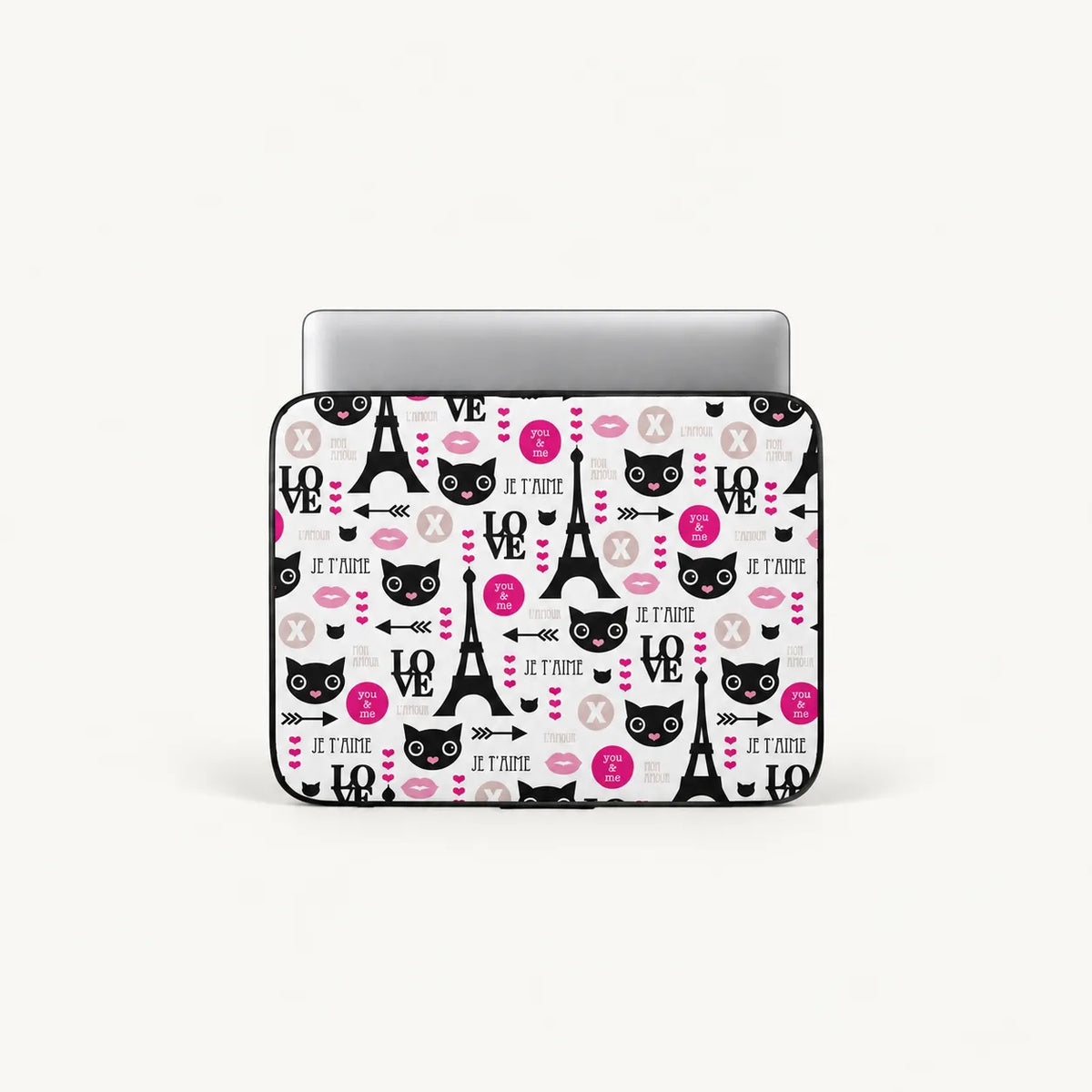 A laptop sleeve featuring a Paris-themed pattern with black cat faces, Eiffel Towers, pink hearts, and the phrase 'Je T'Aime' on a white background, shown with a silver laptop inserted.