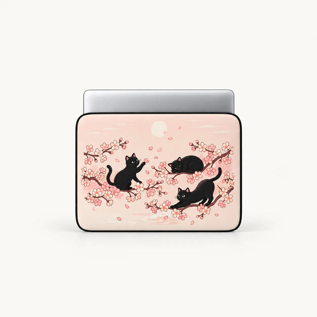 Three black cats playing among Japanese cherry blossom sakura branches on a pastel pink padded laptop sleeve by SLEEVER