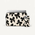 A laptop sleeve and matching phone case set featuring a black bow pattern on a warm cream background, shown on a clean off-white studio background.