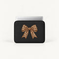 A black laptop sleeve with a large leopard-print bow graphic on the front, shown with a silver laptop partially inserted, against a clean white background.