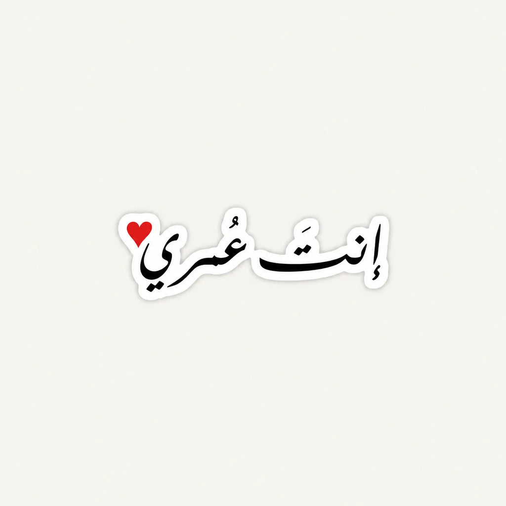 A die-cut sticker featuring Arabic calligraphy in black with a small red heart accent at the top left, outlined in white on a light gray background.