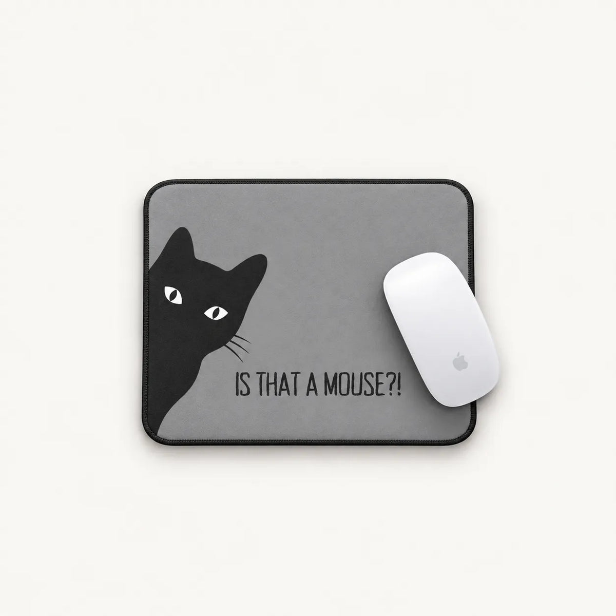 A gray rectangular mouse pad with a black border, featuring a black cat illustration and the text 'IS THAT A MOUSE?!' in black. A white computer mouse rests on the right side of the pad against a clean white background.