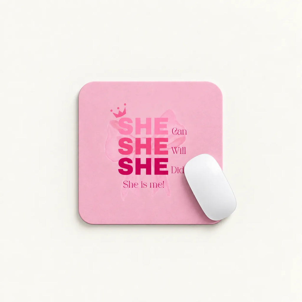 A pink rectangular mouse pad with rounded corners featuring the text 'SHE can SHE Will SHE Did She is me!' in pink and magenta lettering, shown on a light background with a white computer mouse resting on it.