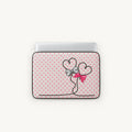 A laptop sleeve featuring a pink and white polka dot pattern with a black line-art heart design tied with a silver bow and a pink ribbon, shown on a light gray background.