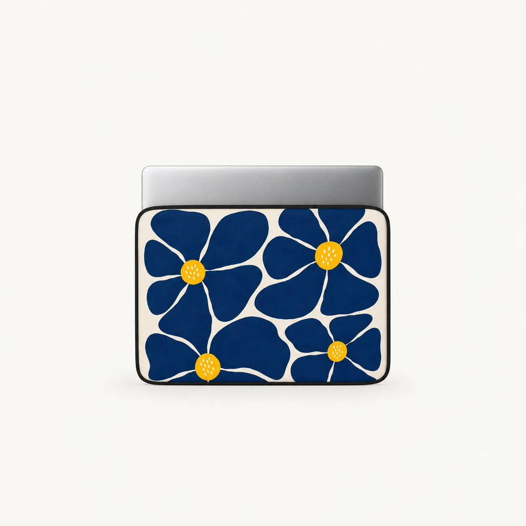 A laptop sleeve featuring a bold navy blue floral pattern with yellow centers on a white background, shown with a silver laptop inserted at the top, set against a clean off-white studio background.