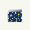 A laptop sleeve featuring a bold navy blue floral pattern with yellow centers on a white background, shown with a silver laptop inserted at the top, set against a clean off-white studio background.