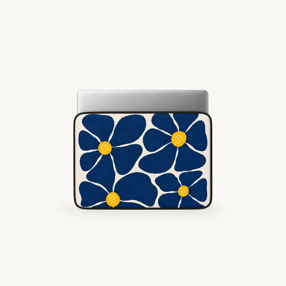 A laptop sleeve featuring a bold navy blue floral pattern with yellow centers on a white background, shown with a silver laptop inserted at the top, set against a clean off-white studio background.