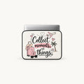 A white laptop sleeve with black trim and a printed graphic featuring the phrase 'Collect moments, not things' in black and pink script, along with illustrations of a pink suitcase, palm tree, airplane, sunglasses, and hearts. A silver laptop is partially inserted at the top, shown on a light gray background.