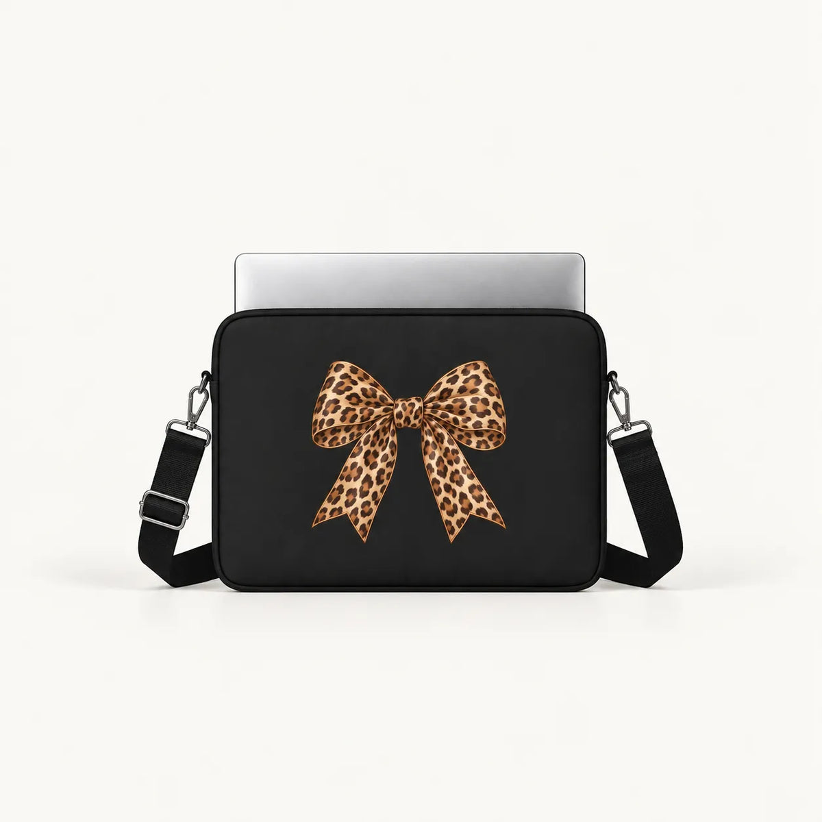 A black laptop sleeve with a large leopard-print bow graphic on the front, shown with a silver laptop inserted at the top, against a clean off-white background.