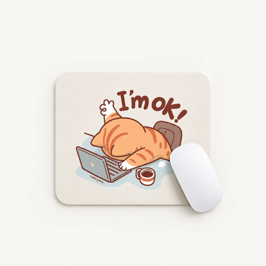 A square mouse pad with rounded corners on a light cream background, featuring a cartoon orange tabby cat sleeping on a laptop with the text 'I'm ok!' and a small coffee cup. A white computer mouse rests on the right side of the pad.