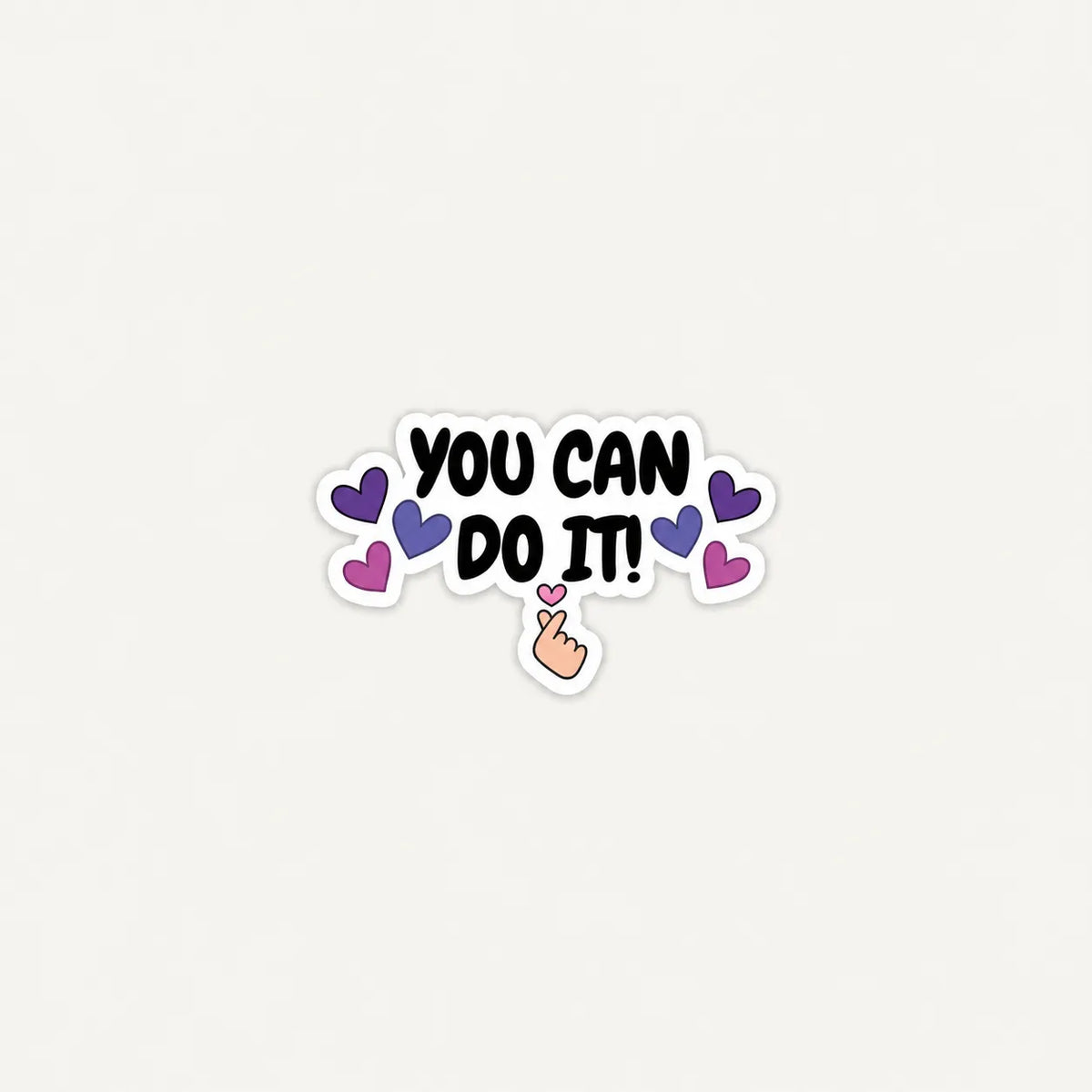 A die-cut sticker with the motivational phrase 'YOU CAN DO IT!' in black lettering, surrounded by purple and pink hearts and a small hand pointing upward, shown on a plain light background.