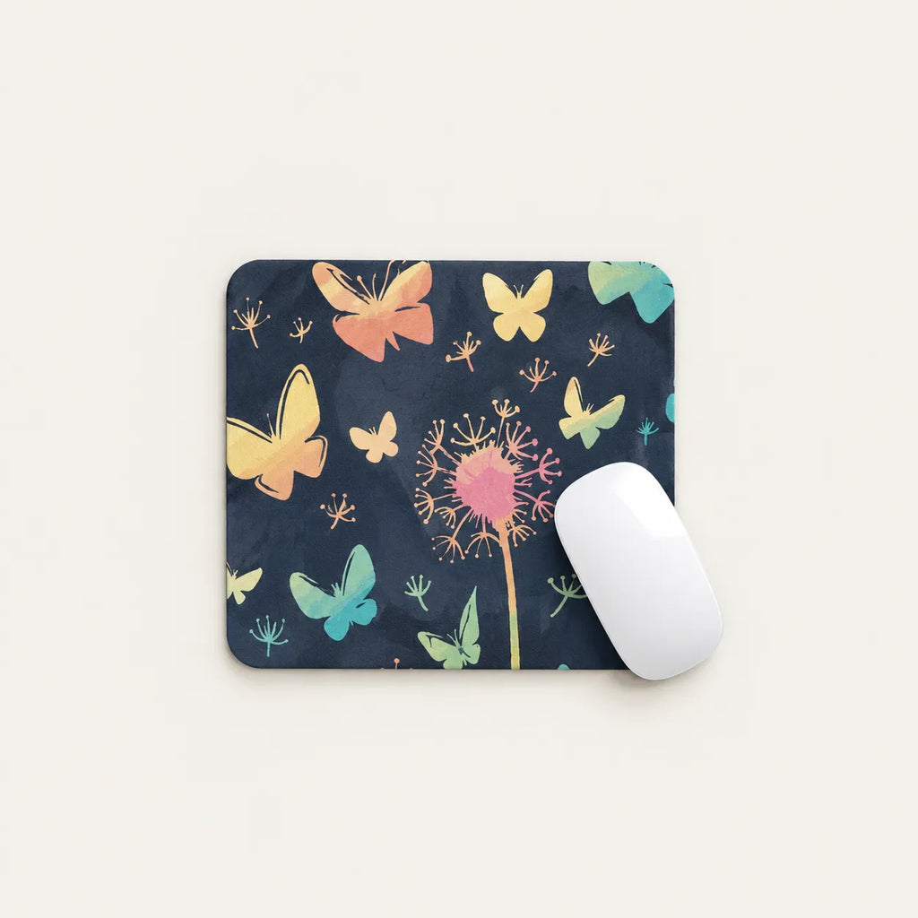 A rectangular mouse pad with a dark navy background printed with colorful butterflies, dandelion details, and small floral motifs, shown on a light beige background with a white computer mouse resting on the right side.
