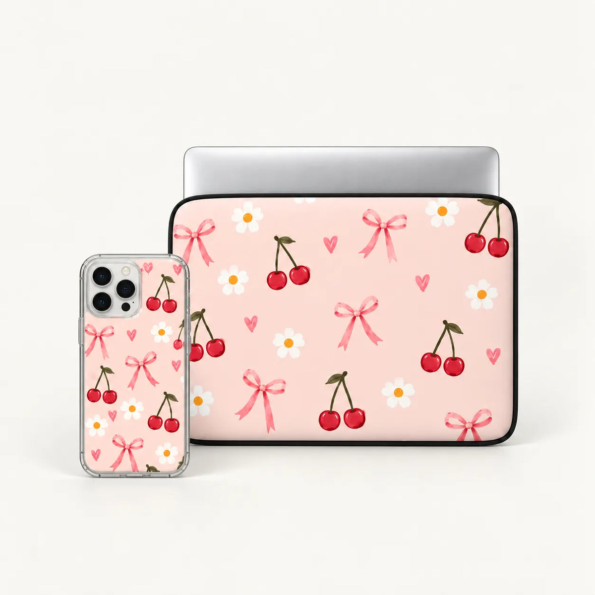 A pink laptop sleeve and matching phone case set with a repeating cherry, bow, and daisy pattern, displayed on a clean white background.