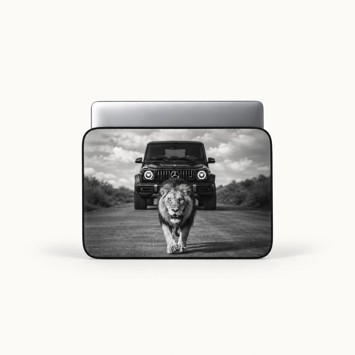 Powerful male lion walking on a road in front of a Mercedes G-Wagon car in dramatic black and white print on a padded laptop sleeve by SLEEVER