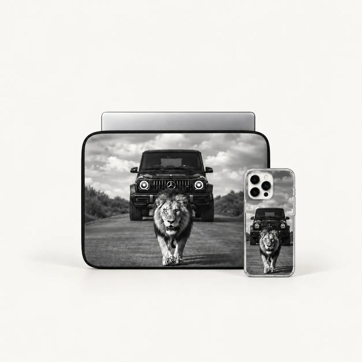 A black laptop sleeve and a clear smartphone case, both printed with a black-and-white safari scene featuring a lion walking toward the camera and a dark off-road vehicle behind it, shown on a light gray background.