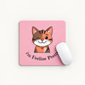 A square pink mouse pad with a cartoon winking orange-and-white cat and the text 'I'm Feeline Pretty' in black script, shown on a light neutral background with a white computer mouse resting on it.