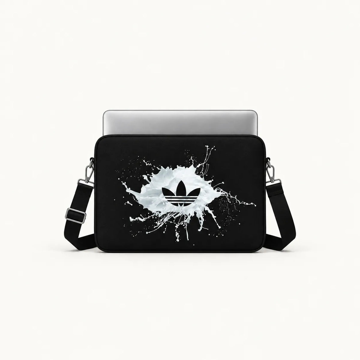 A black laptop sleeve featuring a white paint splatter graphic with a black Adidas trefoil logo in the center, shown with a silver laptop inside on a light gray background.