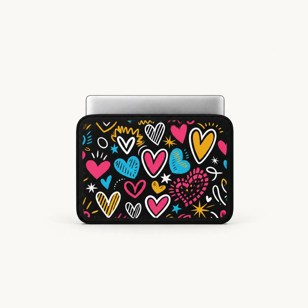 A laptop sleeve featuring a colorful pattern of hand-drawn hearts and doodles on a black background, shown with a silver laptop inserted at the top against a light off-white background.