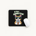 A black rectangular mouse pad with rounded corners on a light beige background, featuring a cartoon orange tabby cat wearing sunglasses and holding a drink under the text 'STAY PAWSITIVE'. A white computer mouse rests on the right side of the pad.