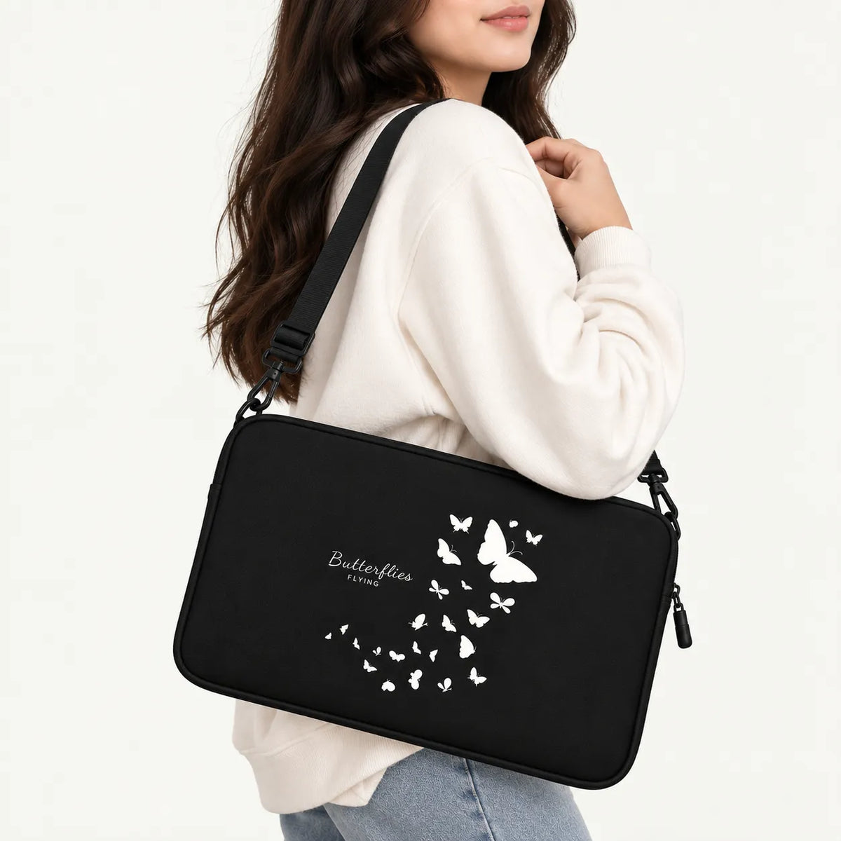 A woman wearing a cream sweatshirt and light blue jeans carries a black shoulder bag with a white butterfly graphic and the text 'Butterflies by now' on the front, set against a plain white background.