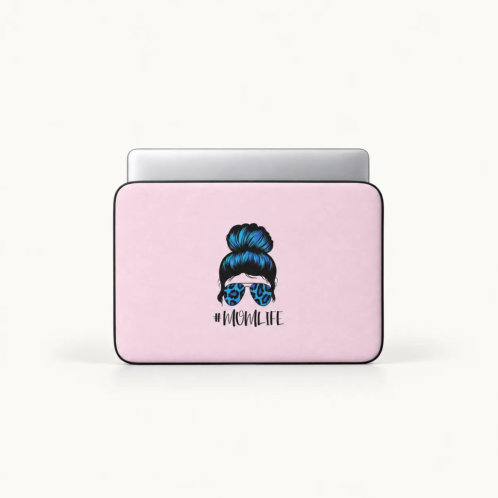 A light pink laptop sleeve with a graphic of a woman's hair in a bun wearing blue leopard-print sunglasses and the text '#MOMLIFE' underneath, shown with a silver laptop inside on a white background.