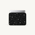 A laptop sleeve featuring a black space design with white stars and constellation patterns, shown with a silver laptop inside on a light gray background.